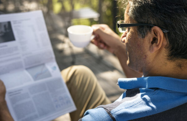 Man relaxing while reading a newspaper and drinking coffee
